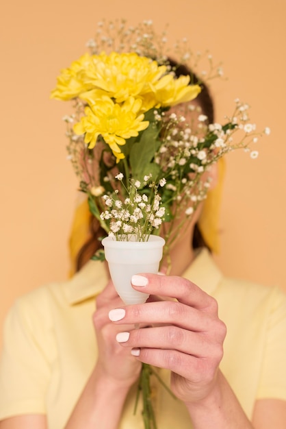 Woman covering face with flowers in plastic cup