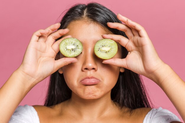 Woman covering her eyes with halves of kiwi