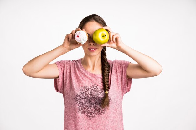 Woman covering her face with cupcake and apple