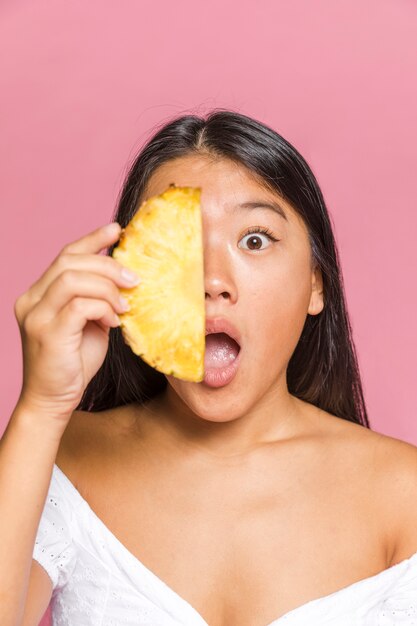 Woman covering her face with slice of pineapple