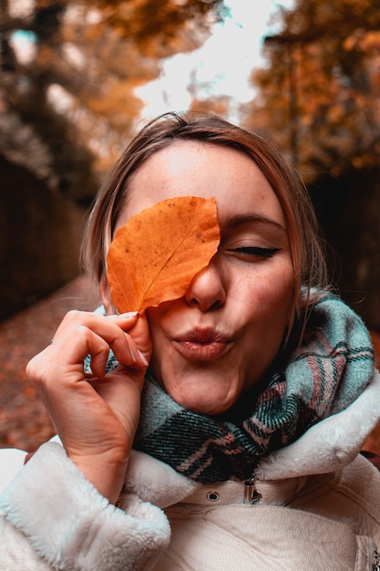 Foto gratuita donna che copre l'occhio destro con foglia marrone