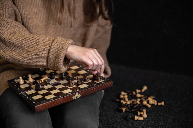 Woman in cozy sweater places wooden chess pieces on a chessboard, copy space.