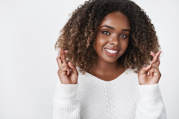 woman cross hands for boyfriend as wishing him luck on match smiling broadly feeling optimistic and hopeful having faith in dream come true posing delighted and joyful over white wall