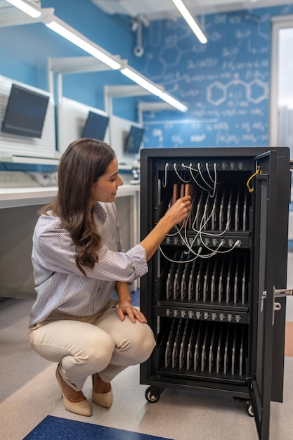 Woman crouched near special cabinet with wires