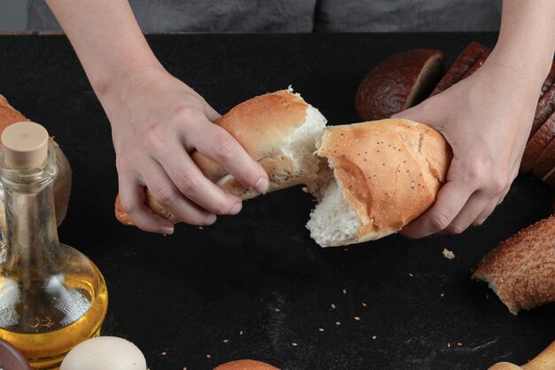 Woman cut bread into half on dark table with eggs and glass of oil.