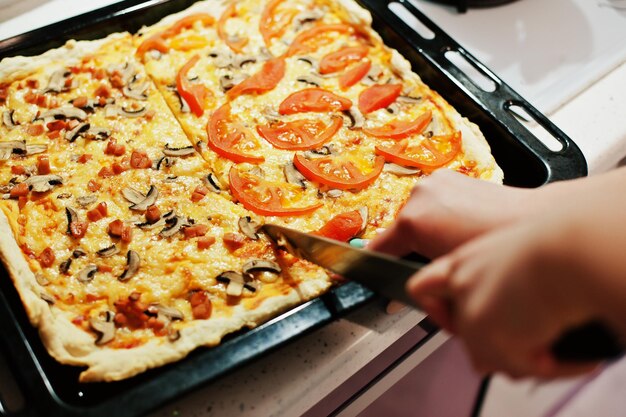 Женщина режет ножом домашнюю пиццу на кухне