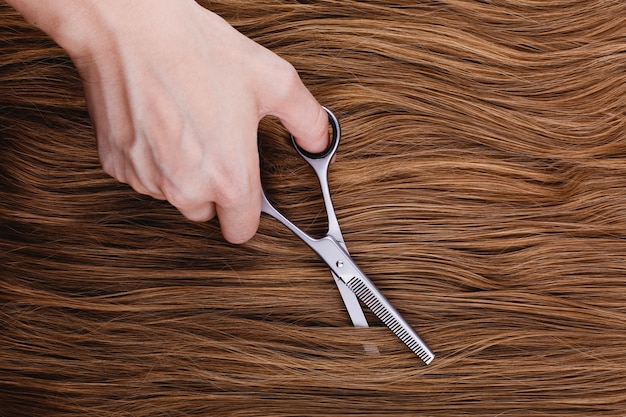 Woman cuts brown hair with steel scissors