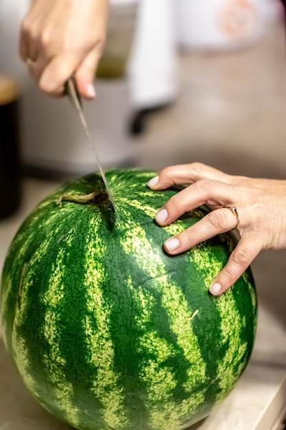 Foto gratuita una donna taglia un'anguria su uno sfondo sfocato della cucina