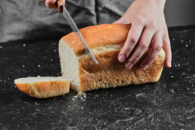 woman cutting bread with knife on dark desk.