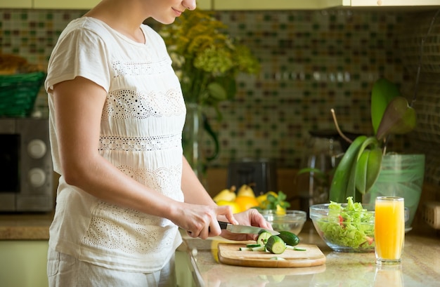 Бесплатное фото Женщина резки огурцов для салата на кухне