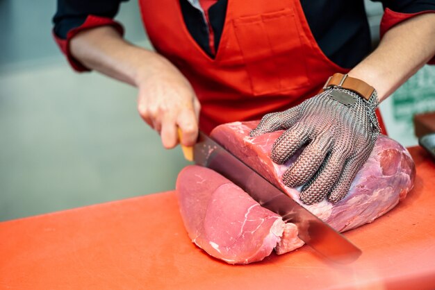 Женщина резки свежего мяса в мясном магазине с металлической защитной сеткой