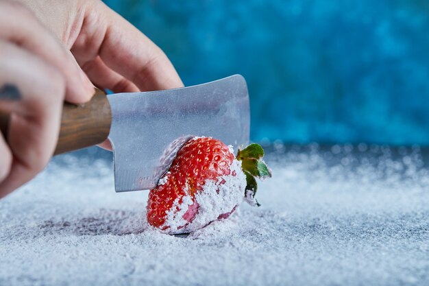 Woman cutting fresh strawberry on blue surface with knife