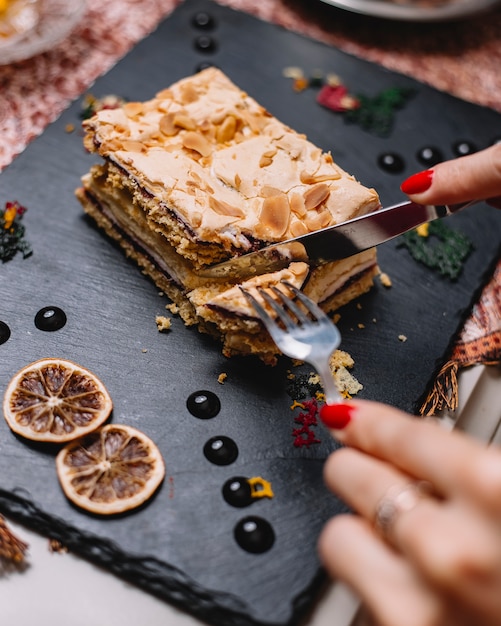 Woman cutting layered raspberry cake with cream and raspberry jam topped with pistachio