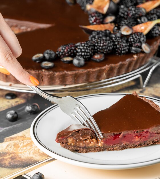 Woman cutting a piece of chocolate cheesecake with raspberry and nuts