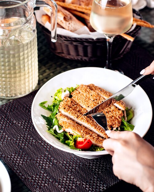 Woman cutting sesame crusted chicken served with salad