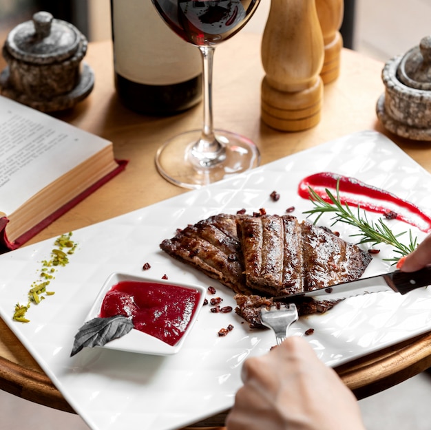 Woman cutting steak piece served with sour sauce