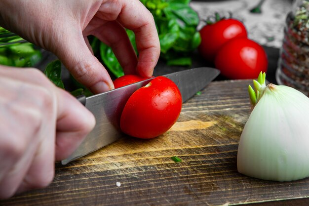 Woman cutting tomato on chopping board close-up.