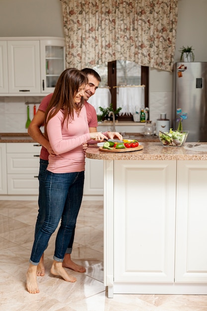 Woman cutting vegetables embraced by her husband