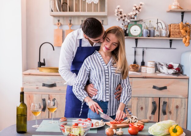 Woman cutting vegetables while man hugging her 