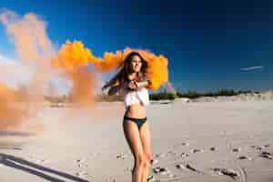 Free photo woman dances with orange smoke on white beach under blue sky