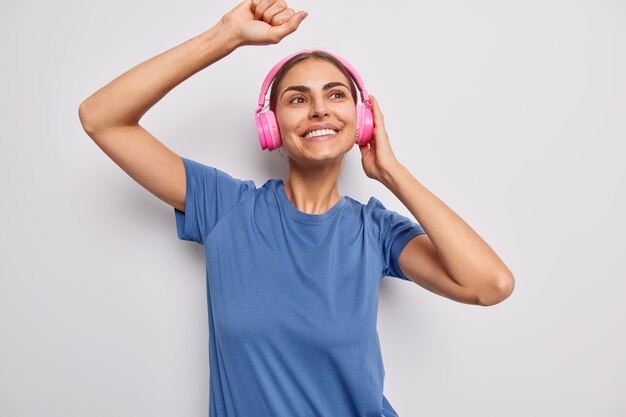 音楽のリズムで踊る女性は、歌のすべてのビットをキャッチします白地にカジュアルな青いTシャツを着たワイヤレスヘッドフォンを着用します