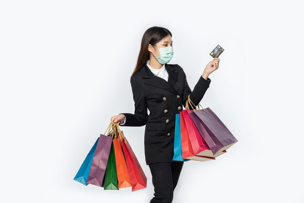 A woman in dark and wearing a mask walks shopping, carries credit cards, and lots of bags