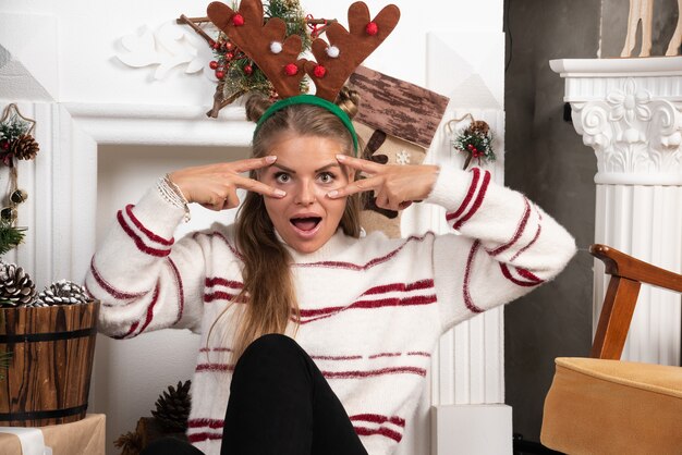 Woman in deer ears looking at front excitedly near the Christmas tree.