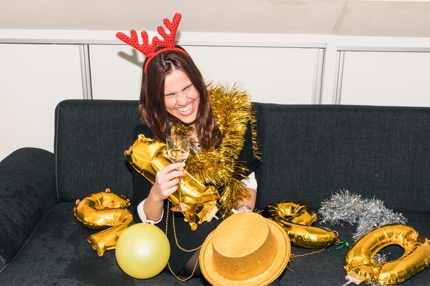 Woman in deer horns sitting on couch with champagne