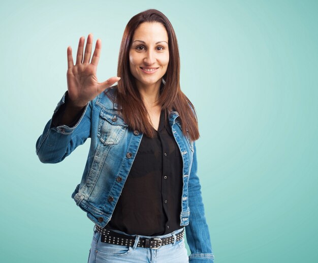 Woman in denim jacket with one hand raised and open