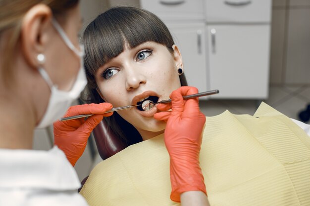 歯科医の椅子に座っている女性。女の子は歯科医によって検査されます。