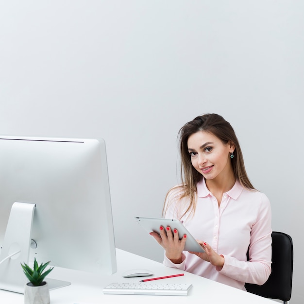 Woman at desk posing while holding tablet