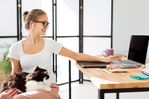 Woman at desk working on laptop and holding cat