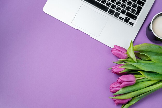 Woman desktop with Laptop morning coffee and tulips on violet background Flat lay Spring holiday Mother day