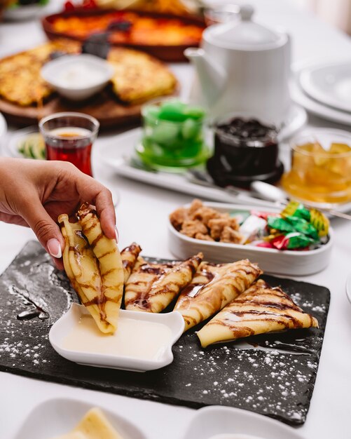 Woman dips crepes with chocolate sauce in condensed milk