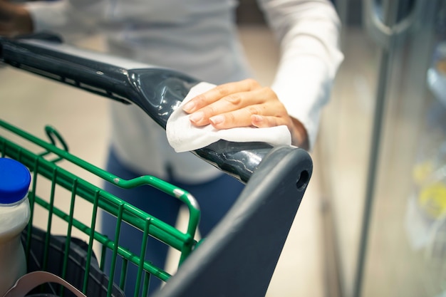 Woman disinfecting shopping cart with sanitizer before use due to corona virus pandemic