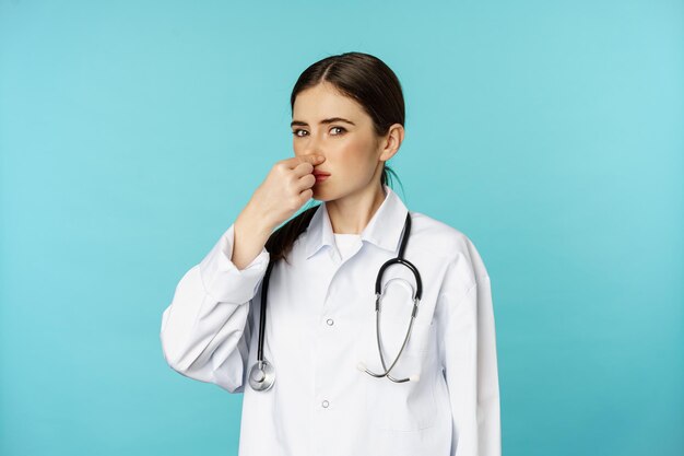 Женщина-врач не любит, закрывает нос от неприятного запаха, воняет, стоит на бирюзовом фоне. Копировать пространство