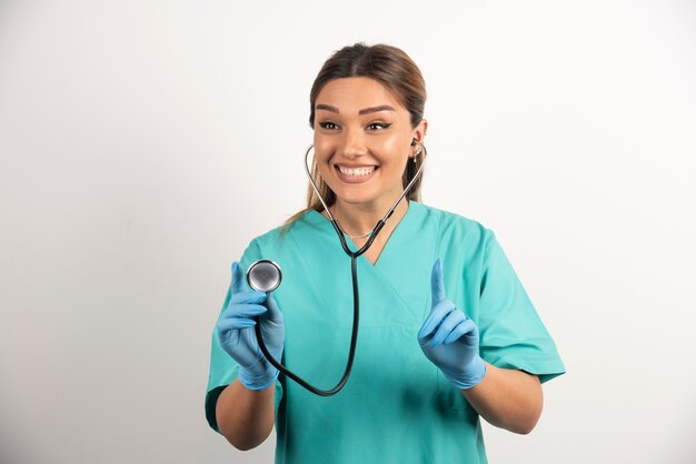 Женщина-врач, стоя со стетоскопом на белом фоне.