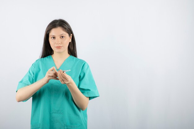 Woman doctor wearing green uniform holding syringe on white. 