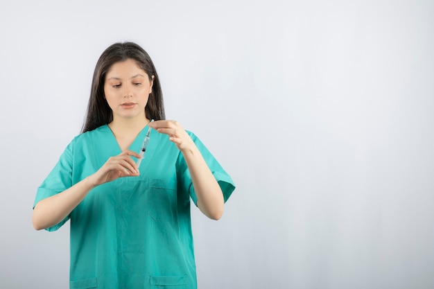 Woman doctor wearing green uniform holding syringe on white. 