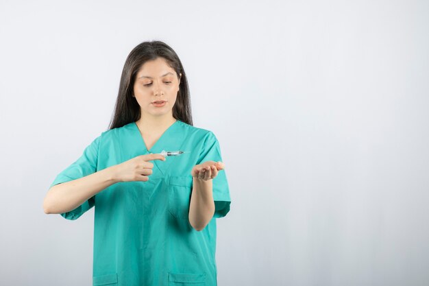 Женщина-врач в зеленой форме, держа шприц на белом.