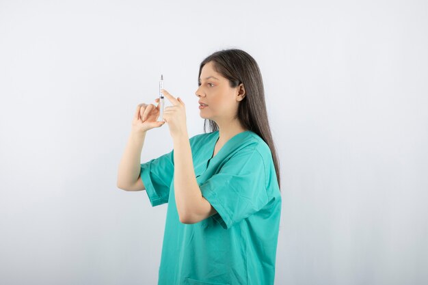 Woman doctor wearing green uniform holding syringe on white. 