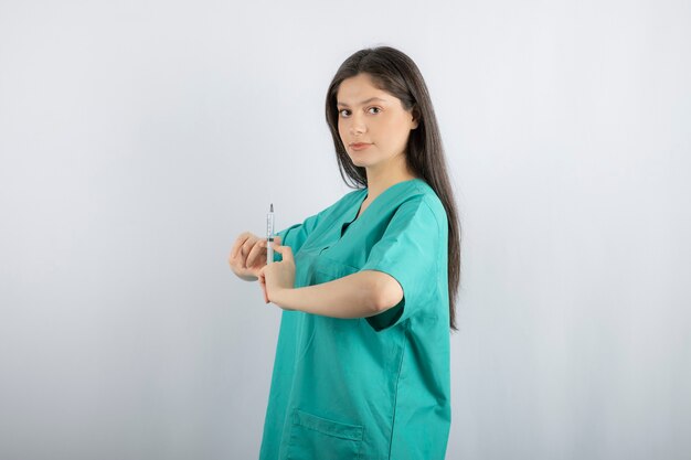 白に注射器を保持している緑の制服を着た女医。