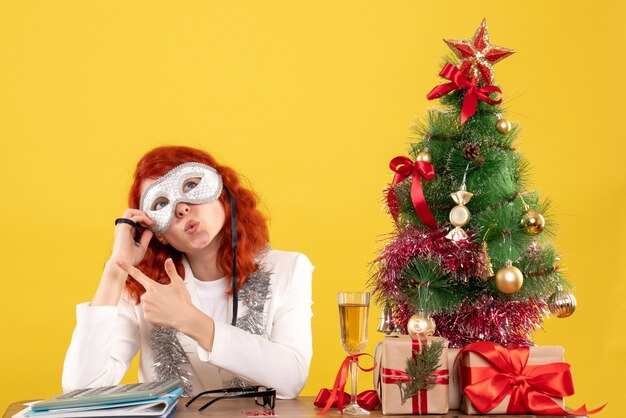 woman doctor wearing mask around christmas tree and presents on yellow