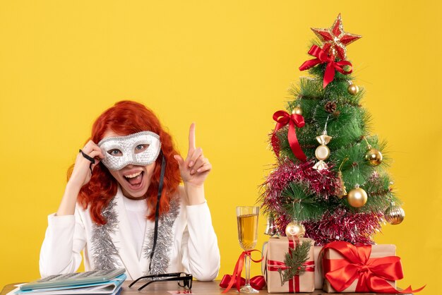 woman doctor wearing mask around christmas tree and presents on yellow