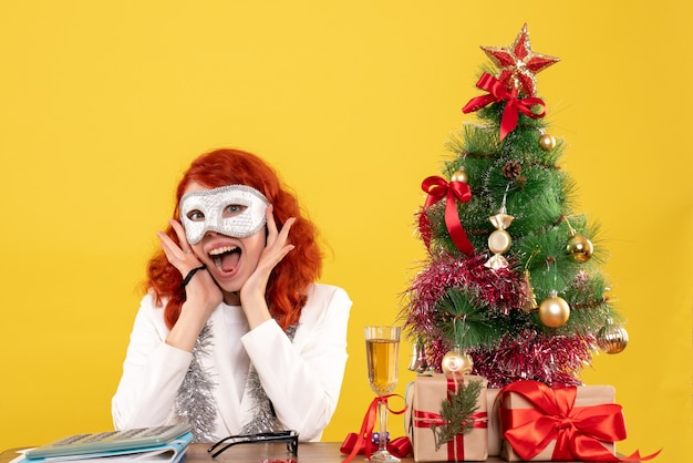 woman doctor wearing mask around christmas tree and presents on yellow