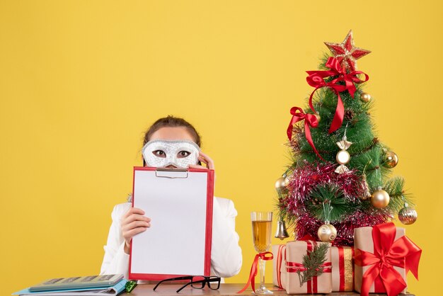 woman doctor wearing party mask and holding file note on yellow