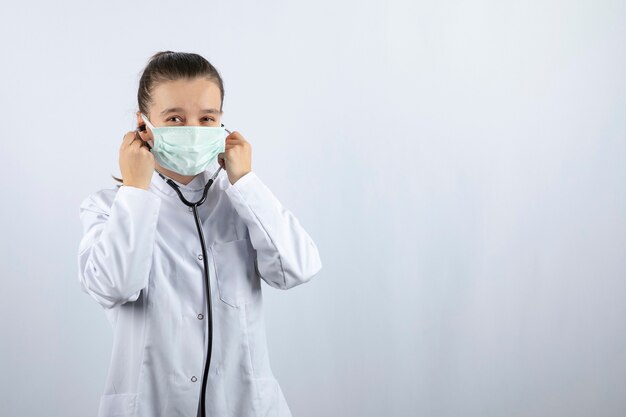 Woman doctor in white uniform wearing a medical mask and holding stethoscope 