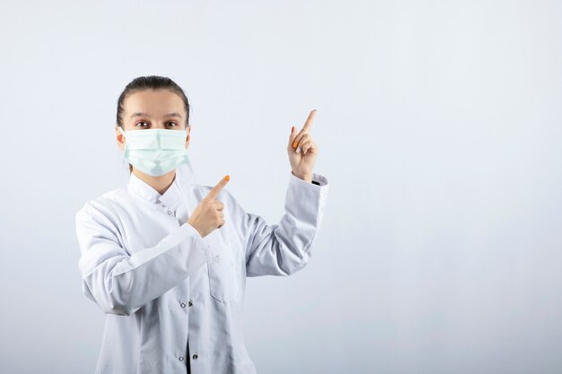 医療マスクを身に着けて、離れて指している白い制服を着た女医