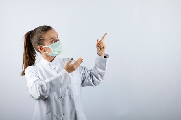 의료 마스크를 착용하고 멀리 가리키는 흰색 제복을 입은 여자 의사