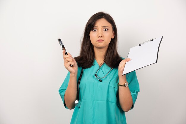 Woman doctor with pen and clipboard looking at camera on white background. High quality photo